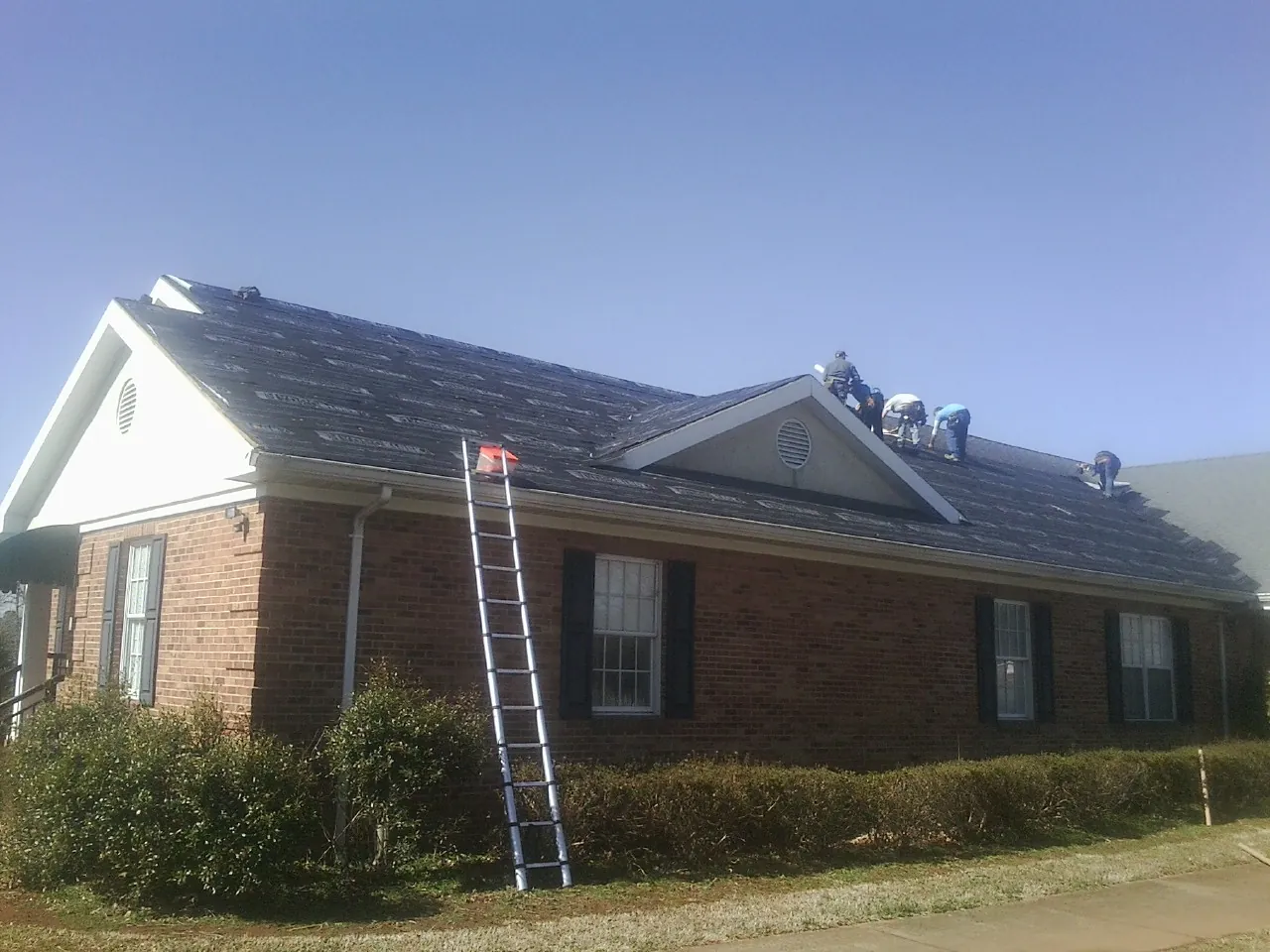 Crew tearing shingles off a brick ranch roof with a ladder set — Emergency Roof Repair work by our crew in Walden