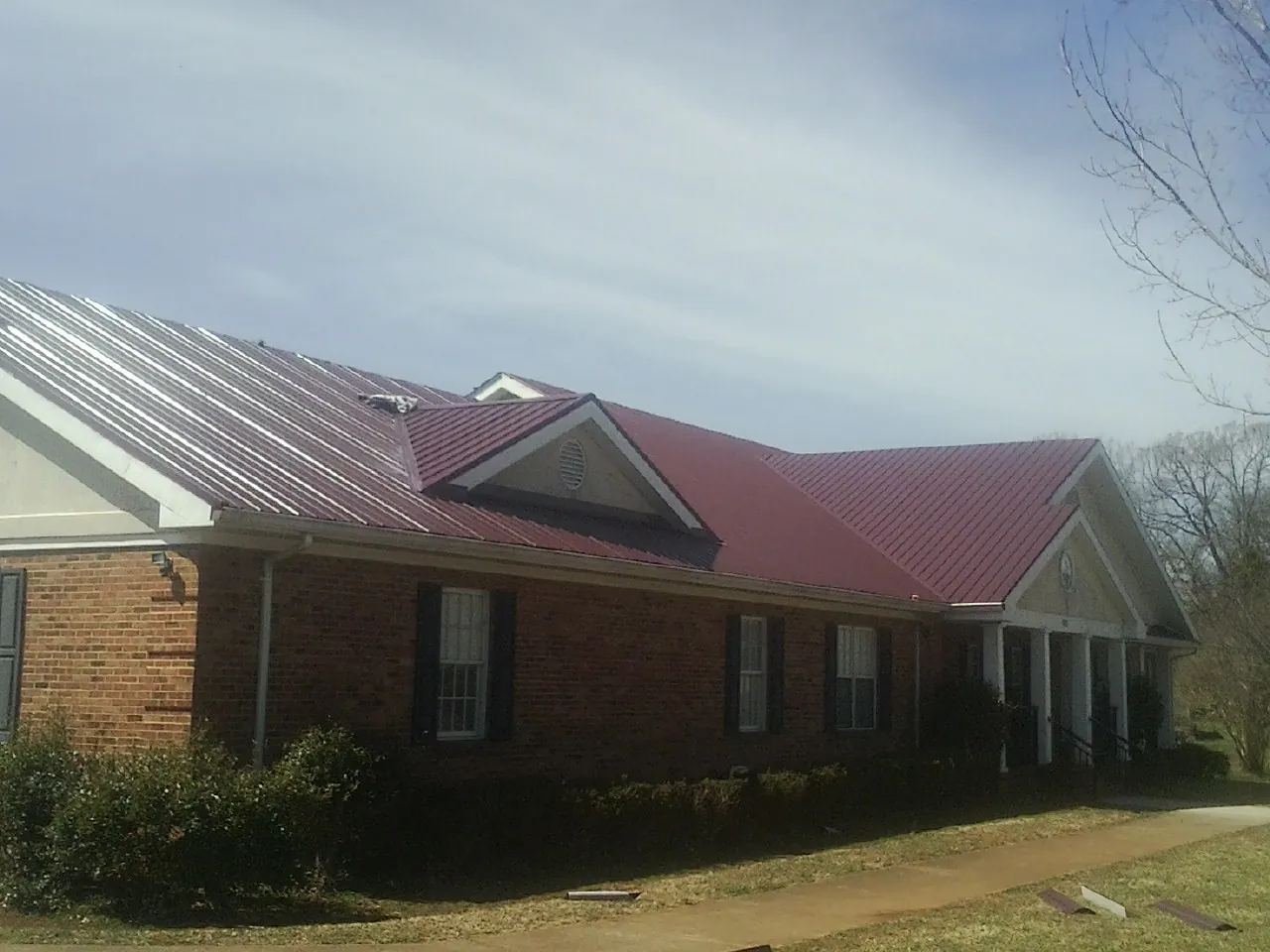 Red metal roof with gabled entries on a long brick building, from a Hail Damage Roof Repair job in Walden