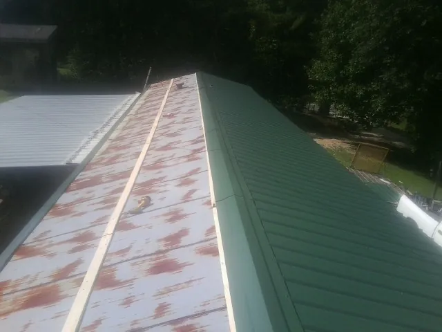 Old rusted panels beside newly installed green metal roofing — Wind Damage Roof Repair by Roofing Brothers in Walden