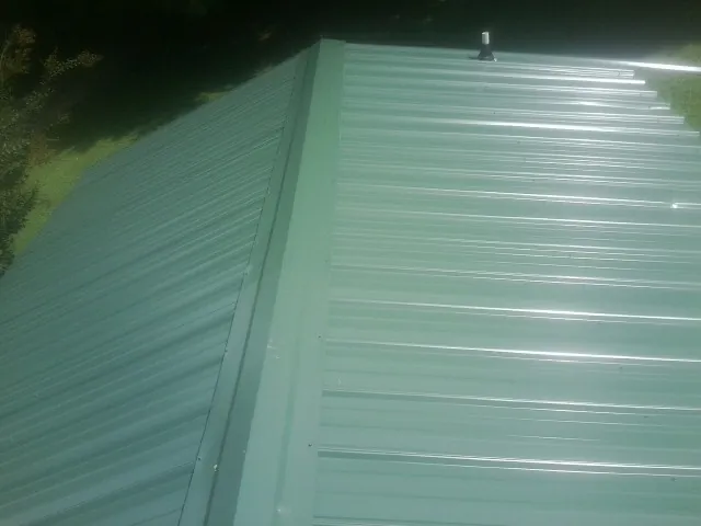 New green metal panels meeting at the ridge of a roof — Flat Roof Repair work by our crew in Walden