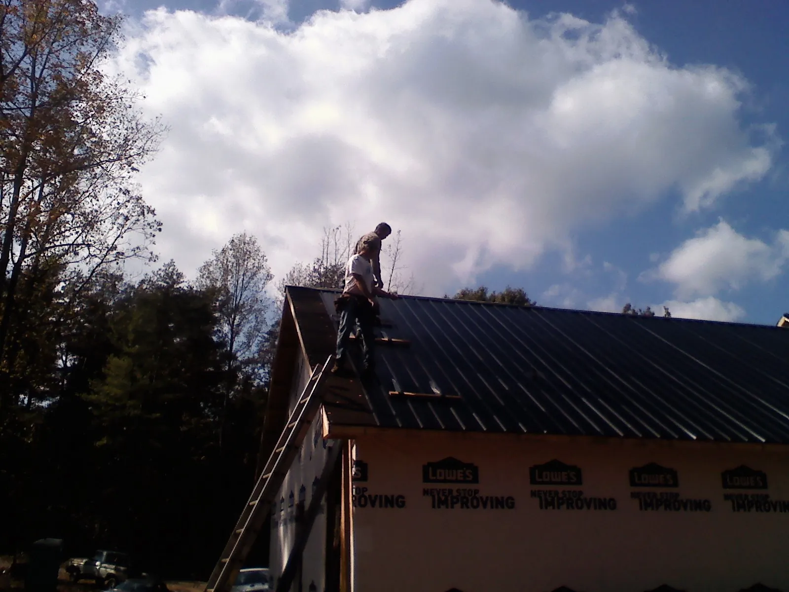 Roofer fastening dark metal panels high against a cloudy sky, from a Roof Inspection job in Walden